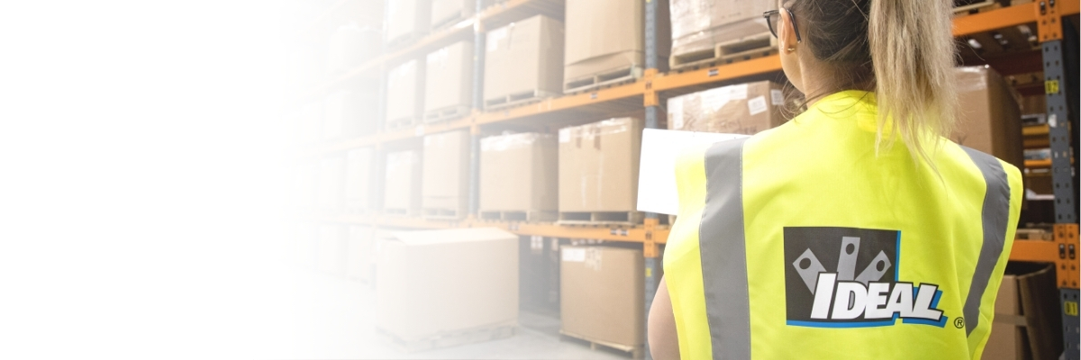 Woman from behind with an IDEA hi-vis vest on looking at rows of cardboard boxes with a white fade on the left